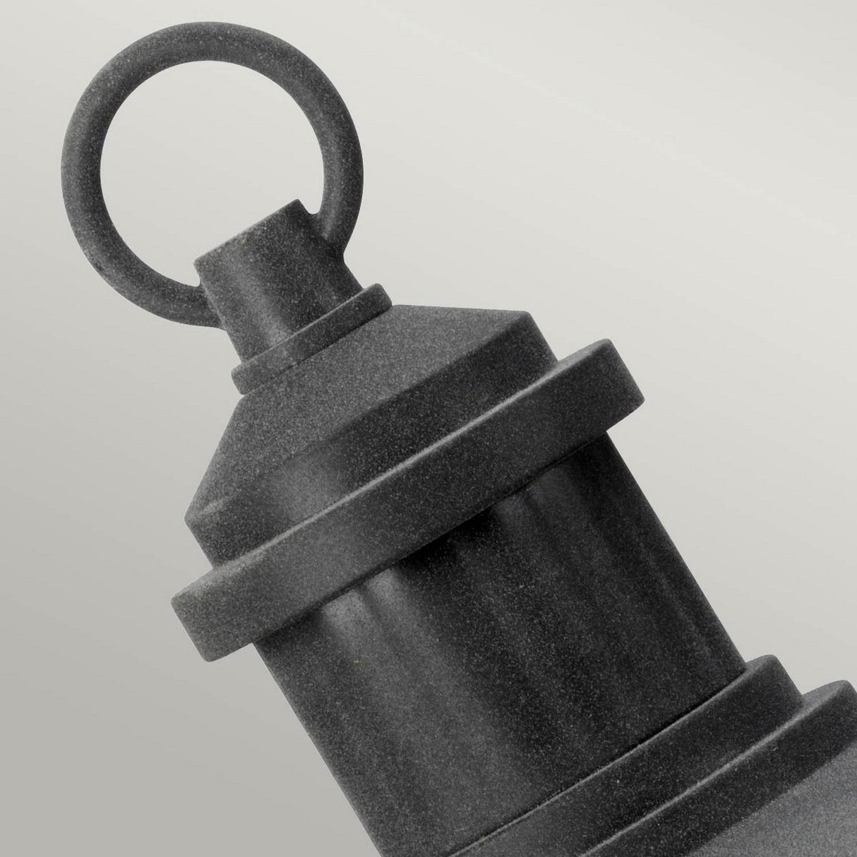 A close-up image of the Riverwood Outdoor 1 Light Pedestal Lantern - Weathered Zinc, showcasing its black, cylindrical form with a circular handle on top against a light gray background. The lantern features a weathered zinc finish and textured surface, evoking an outdoor pedestal lantern or nautical-inspired design.