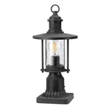 The Riverwood Outdoor 1 Light Pedestal Lantern - Weathered Zinc features a nautical-inspired design with a clear glass case and visible LED bulb. It has a flat, round top and decorative square base, making it ideal for garden or pathway lighting. Its weathered zinc finish adds timeless charm to any outdoor space.