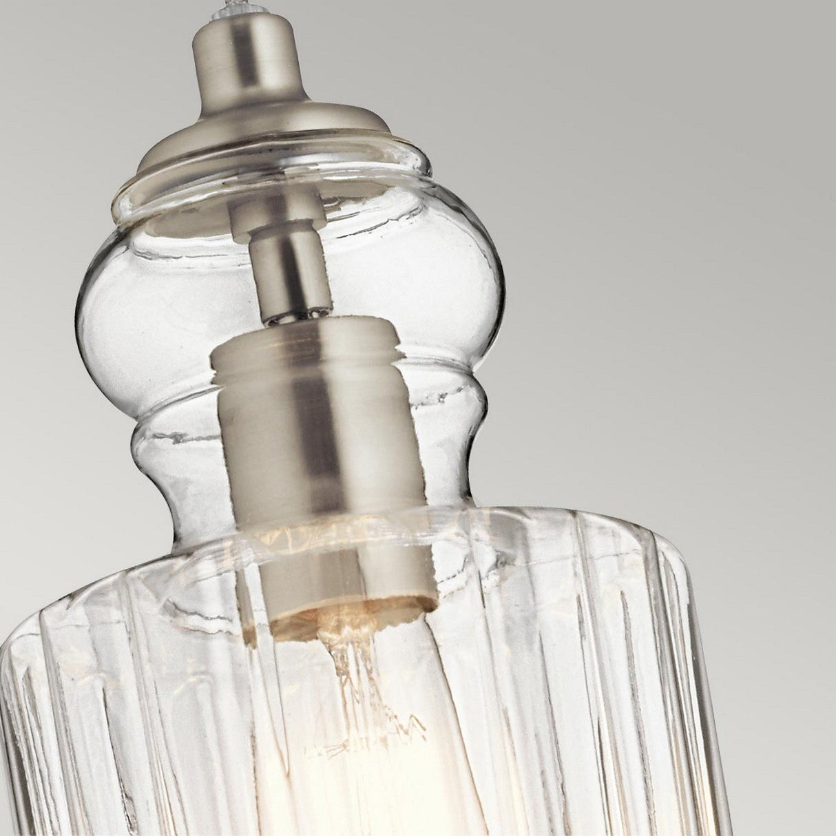 Highlighting the detailed glasswork of the Riviera-2 1 Light Pendant in brushed nickel, this image showcases a vintage-inspired design with ribbed glass and a visible bulb. Set against a simple light gray background, it's an elegant option for kitchen island lighting.