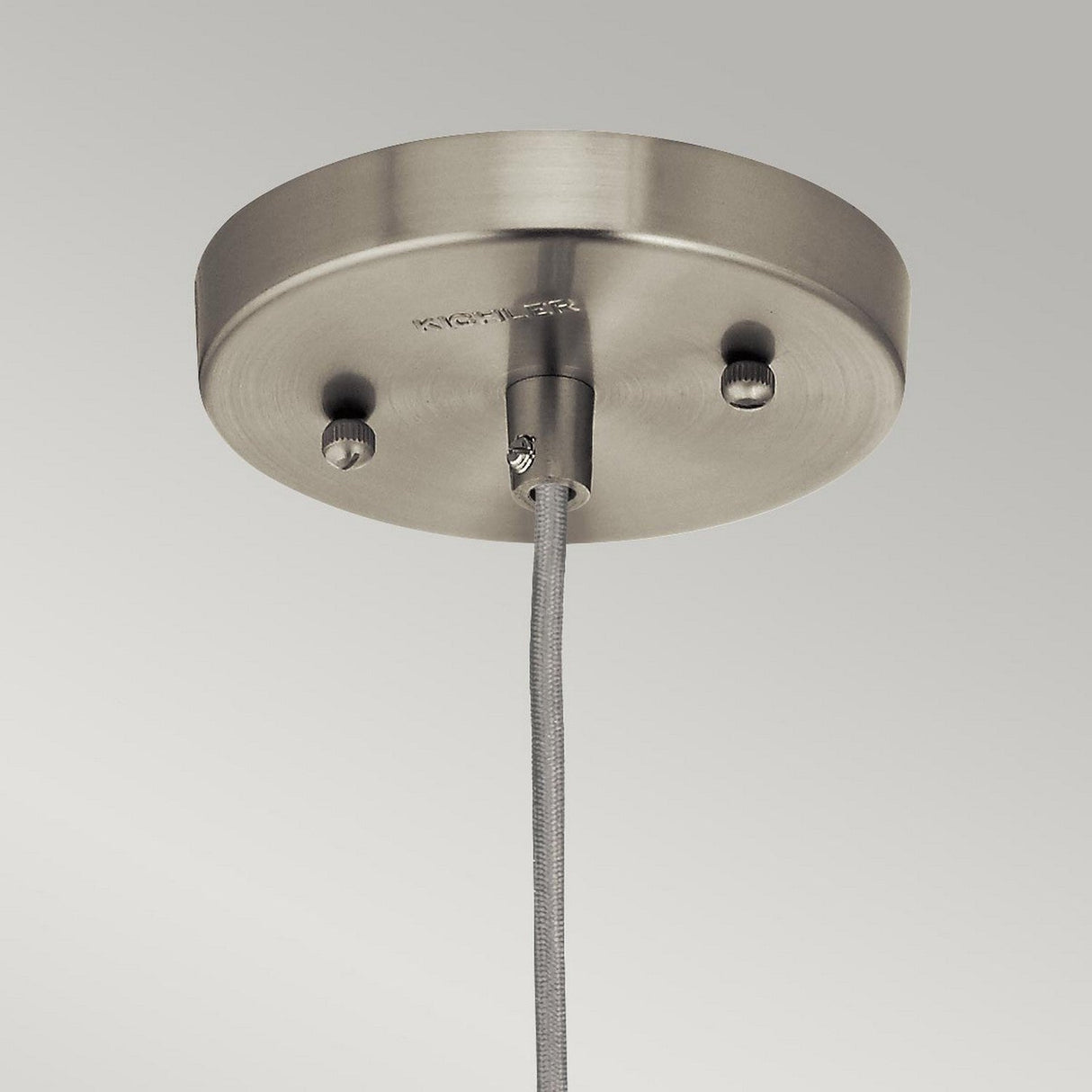 Close-up of the Riviera-2 1 Light Pendant in Brushed Nickel, featuring a round base with two screws on a brushed metal ceiling mount. A cable hangs from the center, secured by a metal fitting that evokes vintage-inspired lighting. The neutral background highlights its minimalist design, making it perfect for kitchen island lighting.