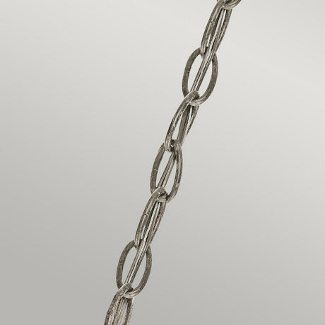 A close-up image of the Rosalie 1 Light Pendant in Sterling Gold, featuring a metal chain suspended diagonally against a plain gray background, evokes the charm of Williamsburg design. The chain consists of interlinked oval-shaped links with a slightly weathered texture, reminiscent of antique mercury glass.