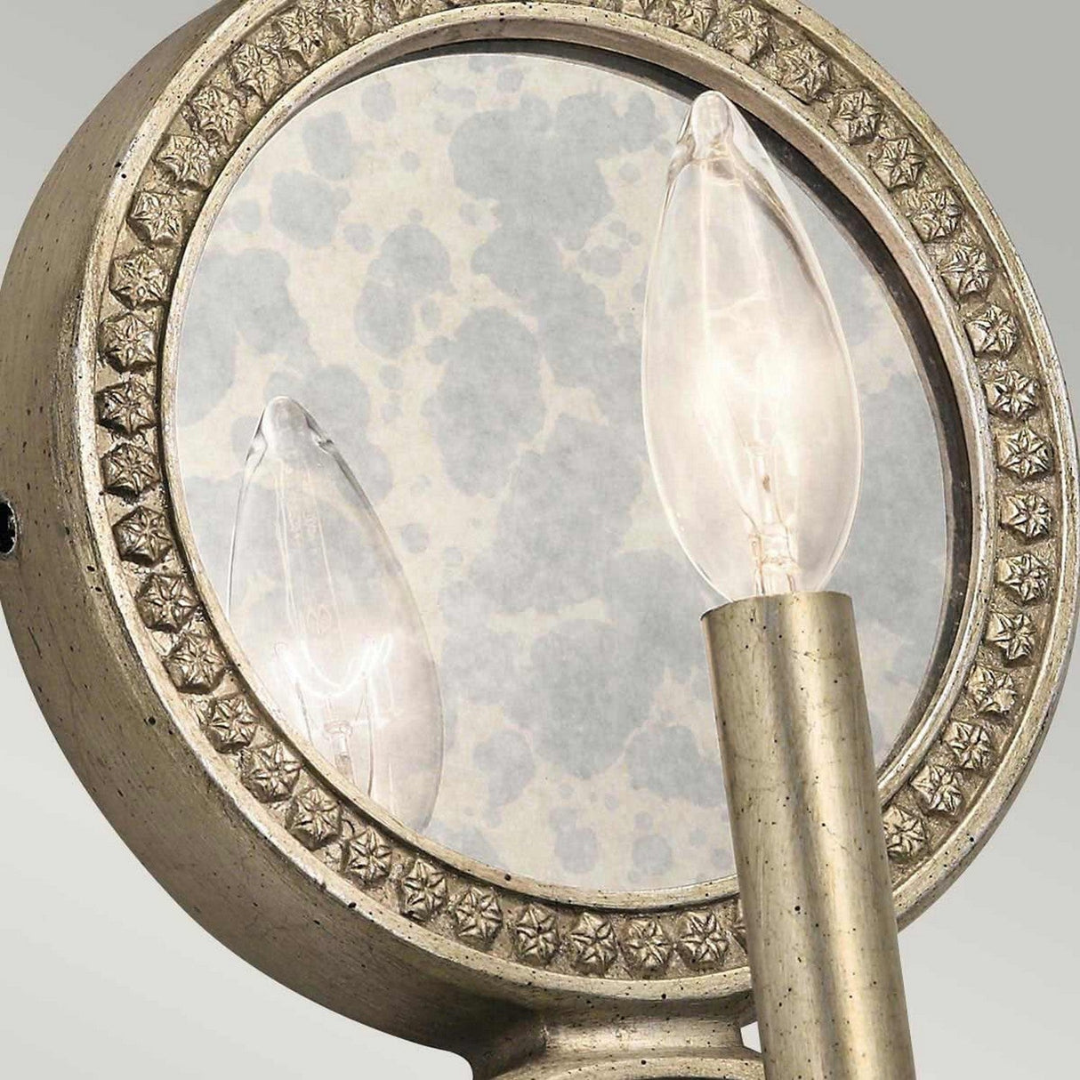 Here's a revised version of the sentence using the given product data:

Close-up of the Rosalie 1 Light Wall Light in Sterling Gold, a decorative sconce featuring one candle-shaped bulb. It boasts a round, patterned backplate with an antique mercury glass finish, lending it an elegant and classic appearance.