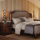 A cozy bedroom with a large bed featuring beige and gray bedding. The walls have vertical beige stripes. Two wooden nightstands with drawers flank the bed, each adorned with a Rosalie 1 Light Wall Light in Sterling Gold and decorative round mirrors. A soft rug lies on the floor.