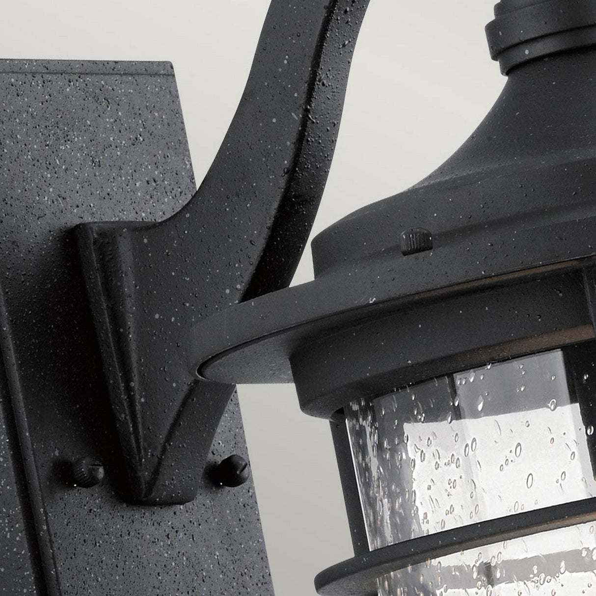 Close-up of the Royal Marine Outdoor 1 Light Medium Wall Lantern in black, featuring a rain-splattered glass cover. This metal fixture exudes vintage appeal with its textured, speckled finish, offering a classic and weathered look that enhances any outdoor lighting setup.