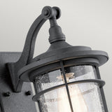 Close-up of the Royal Marine Outdoor 1 Light Small Wall Lantern in black, featuring a curved arm and cylindrical encasement. The seeded glass with a raindrop-like texture enhances its nautical aesthetic. The light inside is turned on, casting a warm glow.