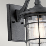 The Royal Marine Outdoor 1 Light Small Wall Lantern in black features a close-up view of its seeded glass, which displays a clear raindrop pattern. Inside, the bulb casts a warm light. The fixture is installed on a rectangular backplate with a simple, modern design that subtly enhances its nautical appearance.