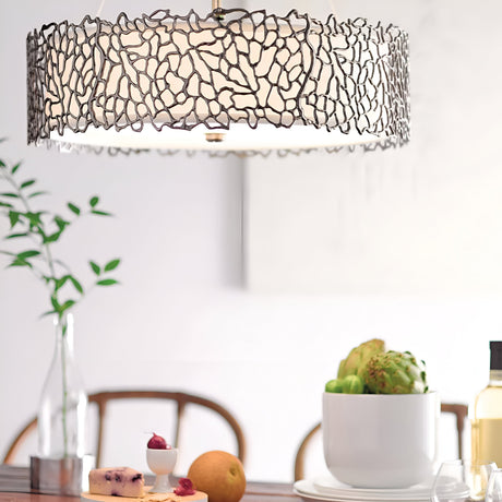 Product Data Rewrite: The Silver Coral 3 Light Pendant/Semi-Flush - Silver, featuring a design that mimics textured metalwork branches, hangs elegantly above a dining table. This modern lighting fixture casts a cozy glow over a display of artichokes, cheese, and an orange in a bowl, alongside a small vase containing a leafy branch. Chairs can be seen in the background.