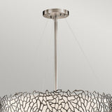 Introducing the Silver Coral 4 Light Drum Pendant - Silver, a modern ceiling light fixture that exudes elegance with its metallic abstract design inspired by nature. This chandelier showcases a metal frame adorned with a wavy, coral-inspired pattern encircling a circular white shade, all supported by a central rod and wires against a plain, light-colored wall.