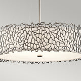 The Silver Coral 4 Light Drum Pendant - Silver features a modern chandelier design with a circular white shade, beautifully encased in an artistic, silver coral-inspired pattern. It hangs gracefully from a central rod against a simple backdrop, capturing nature-inspired elegance.