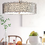A modern dining room features a Silver Coral 4 Light Drum Pendant with a leaf-like design. The table below is elegantly arranged with fruit, cheese, and an artichoke centerpiece. In the background, a plant and wine bottles contribute to the nature-inspired sophistication of the space.