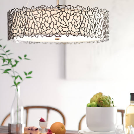A modern dining room features a Silver Coral 4 Light Drum Pendant with a leaf-like design. The table below is elegantly arranged with fruit, cheese, and an artichoke centerpiece. In the background, a plant and wine bottles contribute to the nature-inspired sophistication of the space.