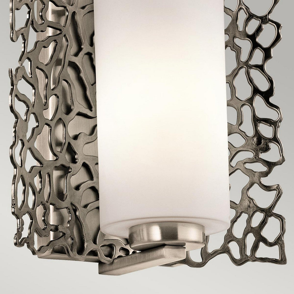 The Silver Coral 1 Light Wall Light - Silver boasts a cylindrical frosted glass shade enveloped in a detailed, nature-inspired metal design. Its brushed finish infuses a contemporary flair into this elegant piece of decorative lighting, echoing organic shapes found in the natural world.