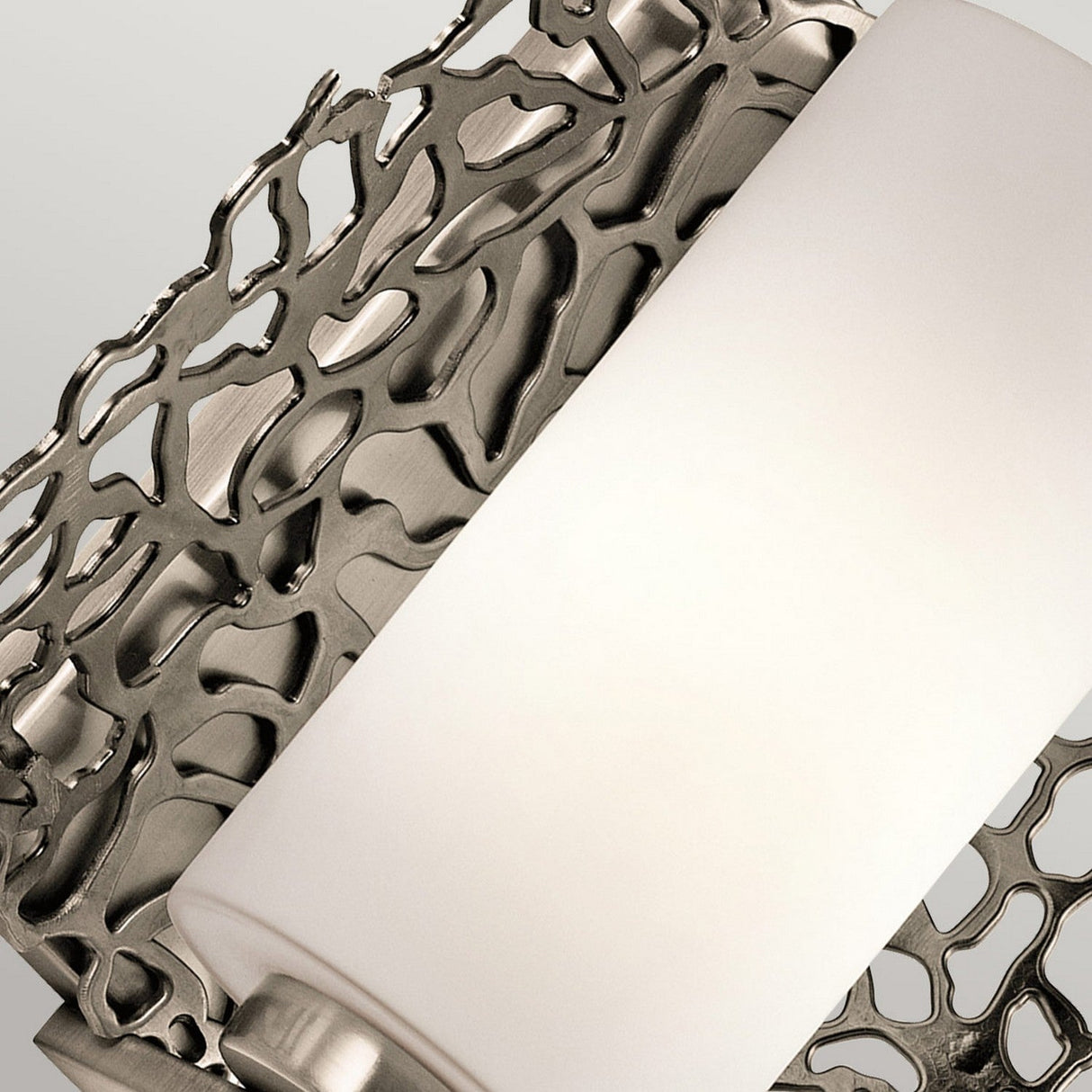 Close-up of the Silver Coral 1 Light Wall Light in silver, featuring a cylindrical white fixture on an elaborate metallic lattice design. The nature-inspired aesthetic is accentuated by a soft gray background that highlights the textured metalwork pattern.