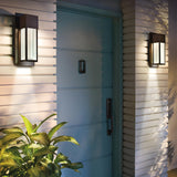A teal front door with a silver handle is set against a light-colored, horizontally paneled wall. Two Sorel Outdoor 1 Light Wall Lanterns in bronze illuminate the doorway, and a potted plant with green leaves is positioned on the left.