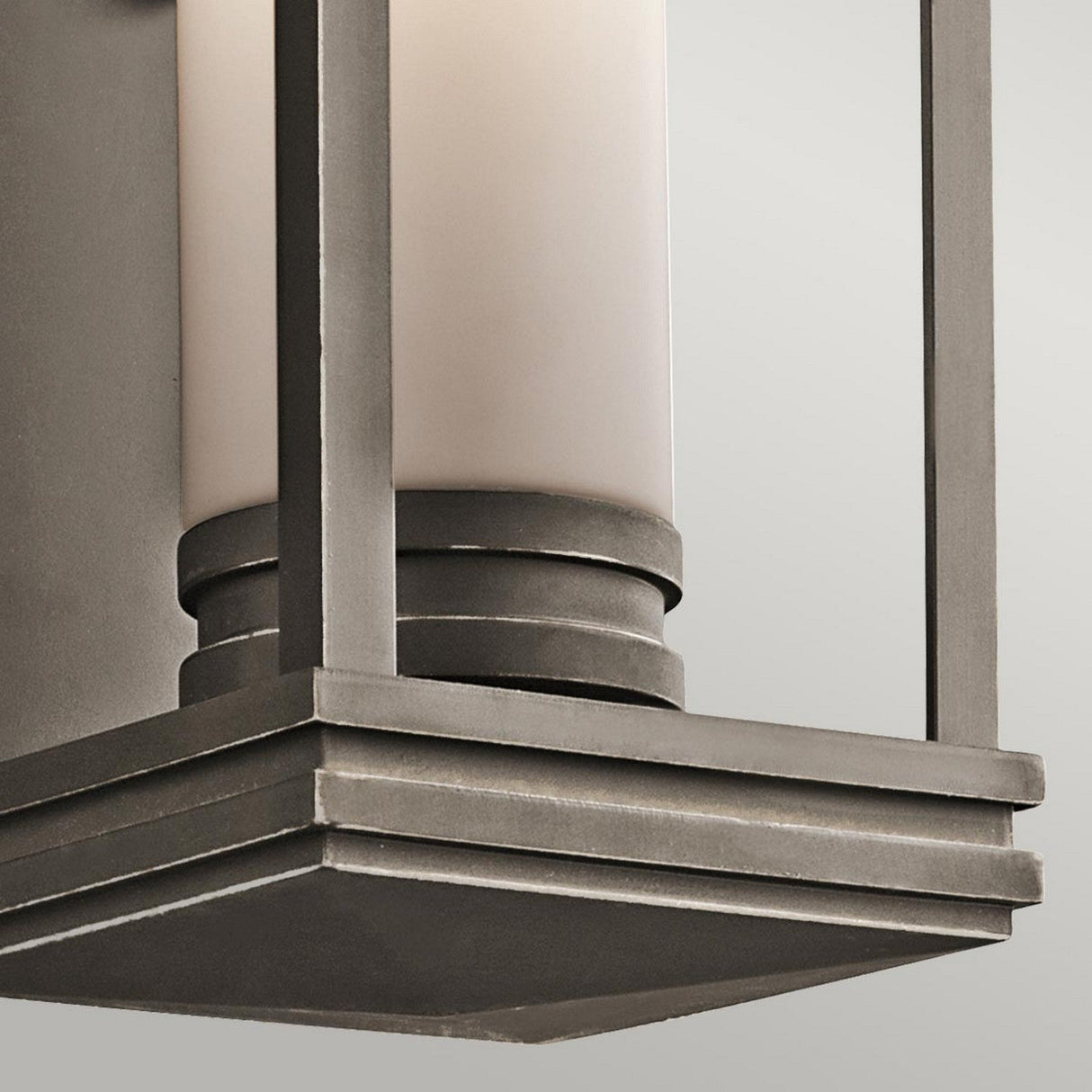 A detailed view of the South Hope Outdoor 1 Light Medium Wall Lantern showcases its modern design, featuring a rectangular metal frame in a rubbed bronze finish. The frame elegantly encloses an opal glass cylindrical light shade, all set against a light gray background.