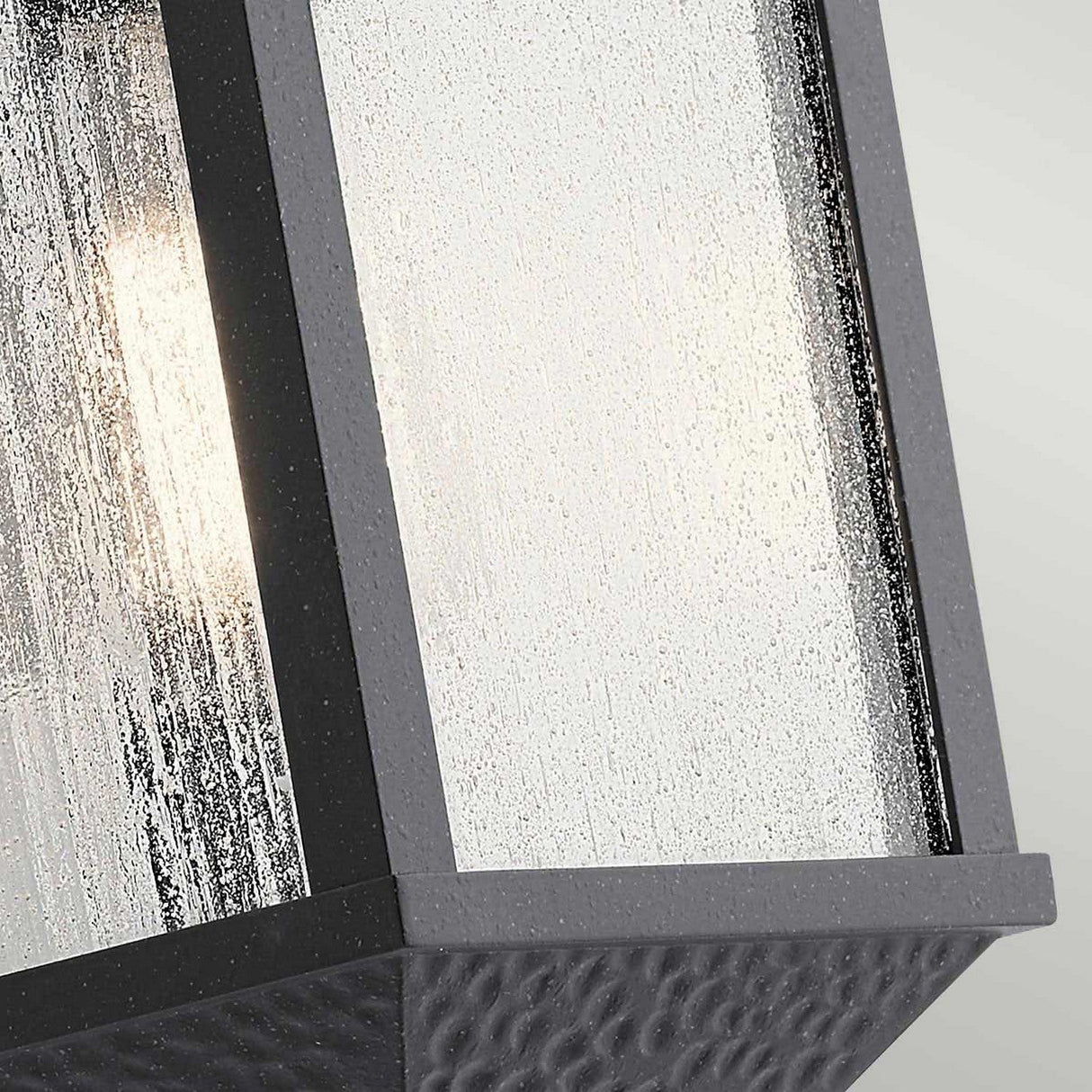 A close-up of the Springfield Outdoor 1 Light Small Wall Lantern showcases its distressed black finish and textured glass pane. Its IP44-rated design ensures durability, while the interior light provides a faintly visible, soft glow.
