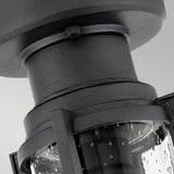 Close-up of the Suri Outdoor 1 Light Porch/Pedestal Lantern in black, showcasing its textured lantern design with a cylindrical glass cover adorned with water droplet patterns. This fixture, radiating nautical charm, is mounted against a light gray background.
