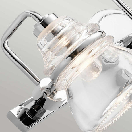 Close-up of the Talland 3 Light Wall Light - Polished Chrome, displaying its contemporary design with a clear glass shade. The bathroom fixture is angled downward, highlighting its sleek style against a light gray background.