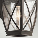 Close-up of the Tangier Outdoor 1 Light Medium Wall Lantern in Olde Bronze, featuring a black metal frame and clear glass panels textured with water droplets. Inside, a glowing bulb emits a warm light, and the lantern boasts an IP44 rating for weather-resistant durability.
