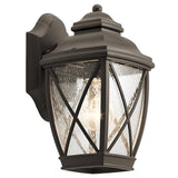 Introducing the Tangier Outdoor 1 Light Small Wall Lantern in Olde Bronze, featuring a classic design with clear, textured glass panels and a crisscross pattern. This decorative lantern is mounted on a wall bracket and beautifully illuminates its surroundings, adding charm to any setting.
