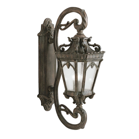The Tournai Outdoor 4 Light Grand Wall Lantern - Bronze is an ornate, vintage-style outdoor wall lantern with intricate scrollwork and seedy glass panels, mounted on a decorative wall bracket.