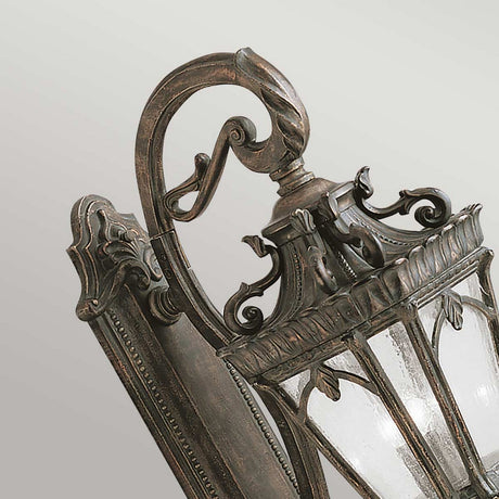 Detailed view of the Tournai Outdoor 4 Light Grand Wall Lantern in a weathered bronze finish, featuring ornate metalwork with intricate leaf and scroll designs complemented by seedy glass panels.