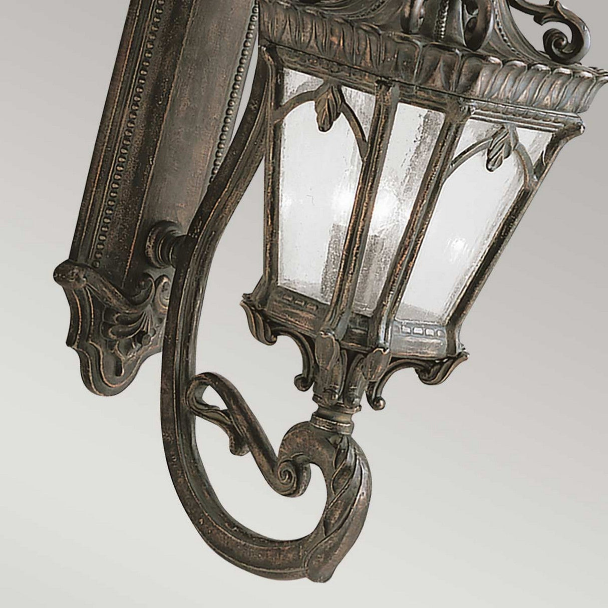 A close-up of the Tournai Outdoor 4 Light Grand Wall Lantern - Bronze highlights its intricate metalwork and classic design. The lantern boasts a dark bronze finish paired with seedy glass panels, elegantly affixed to a decorative wall mount.