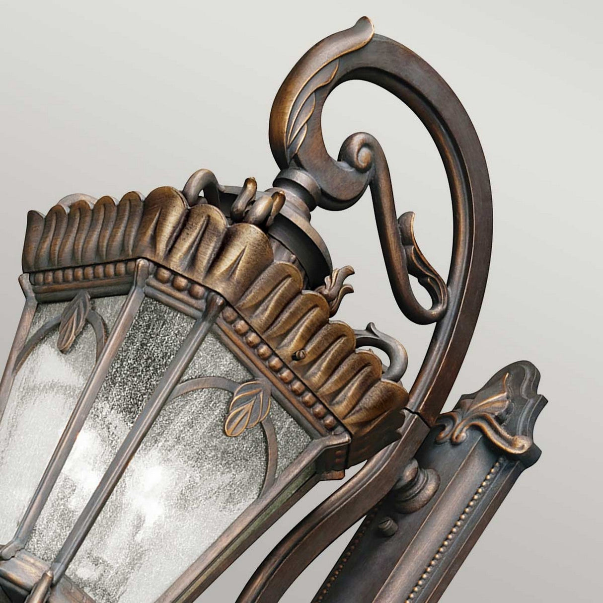 The Tournai Outdoor 4 Light Grand Extra Large Wall Lantern in bronze showcases intricate metalwork with decorative leaf designs, complemented by seedy glass panels. The elegant lantern's vintage touch is enhanced by its bronze finish, standing out beautifully against a soft gray background.