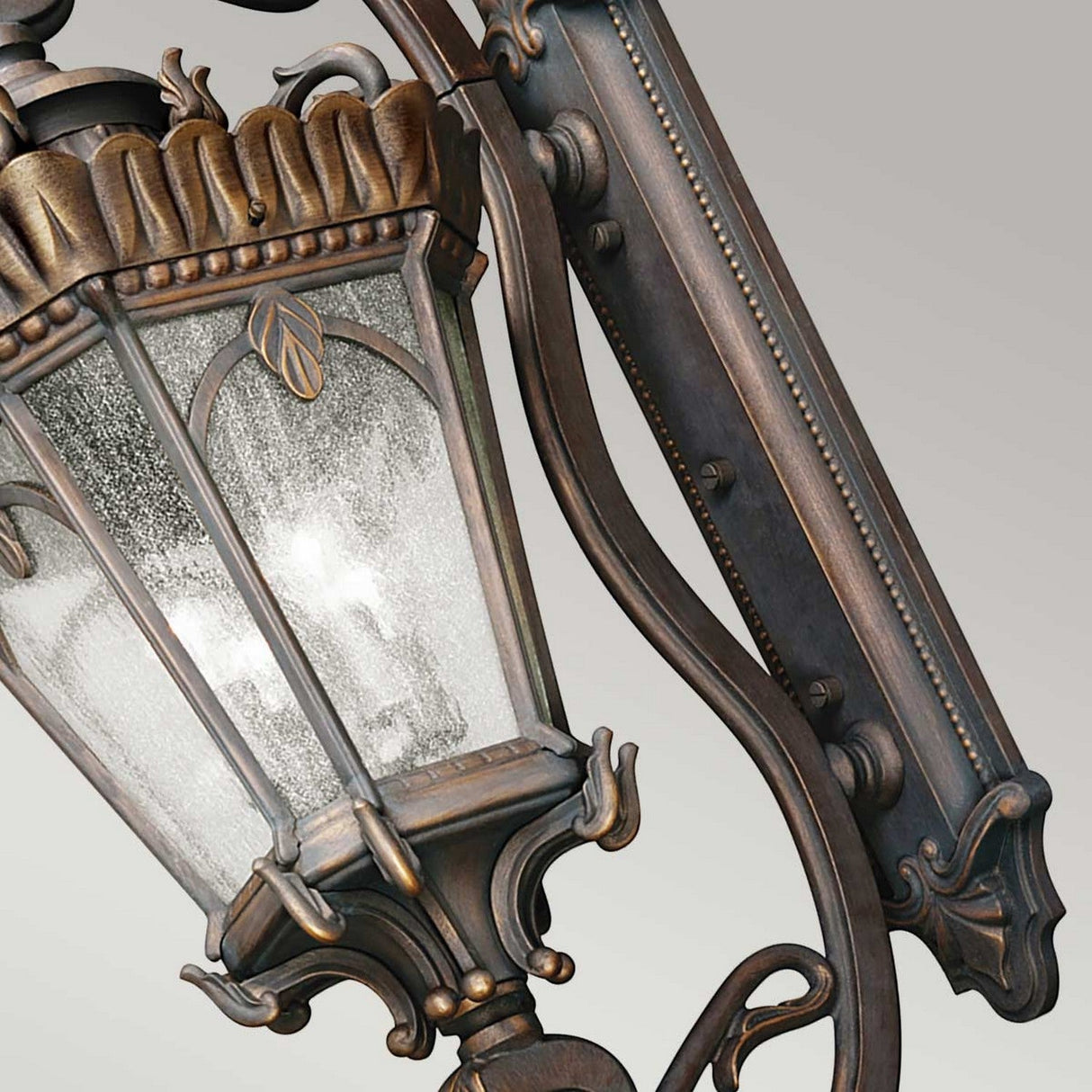 The Tournai Outdoor 4 Light Grand Extra Large Wall Lantern in bronze boasts intricate leaf designs and seedy glass panels, adding a vintage aesthetic against a neutral background.