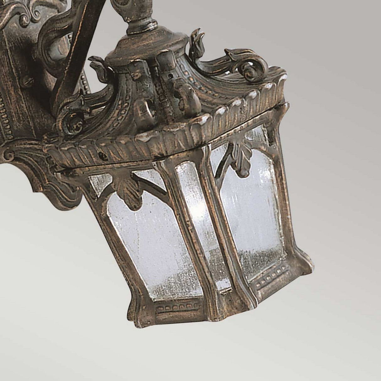 The Tournai Outdoor 1 Light Small Wall Lantern - Bronze features an antique-style design with a decorative, ornate metal frame and square glass panels. Its weathered bronze finish offers vintage appeal, elegantly mounted on a wall bracket.