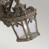 The Tournai Outdoor 1 Light Small Wall Lantern - Bronze features an antique-style design with a decorative, ornate metal frame and square glass panels. Its weathered bronze finish offers vintage appeal, elegantly mounted on a wall bracket.