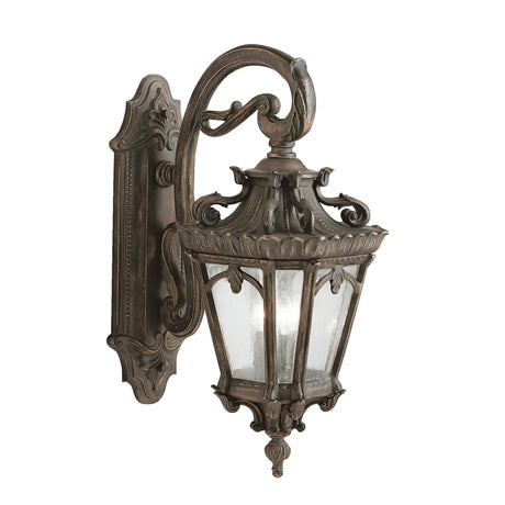 The Tournai Outdoor 3 Light Extra Large Wall Lantern in bronze features intricate scrollwork with a classic lantern-style design, complemented by seedy glass panels and a decorative wall mount bracket for an elegant touch.
