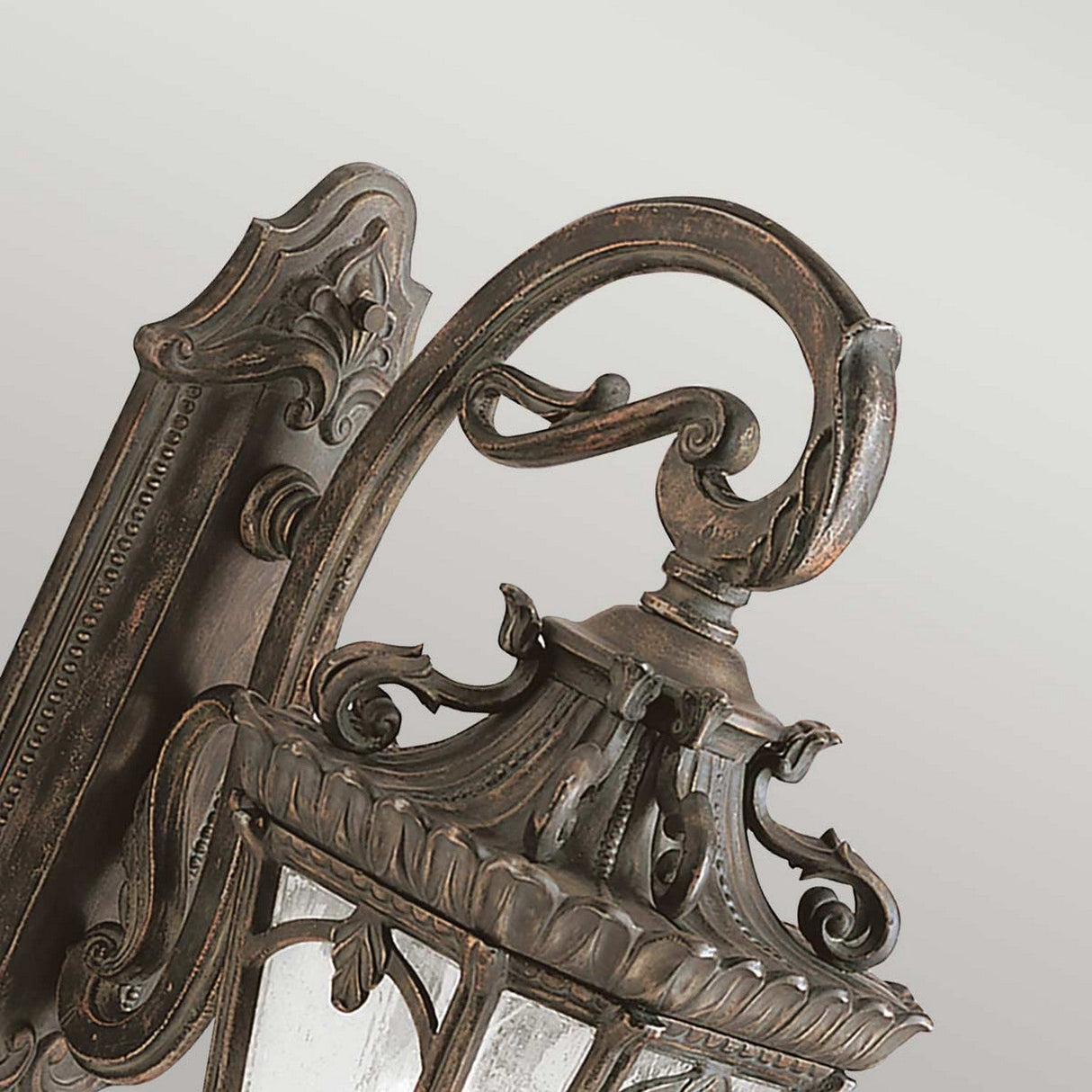 A detailed view of the Tournai Outdoor 3 Light Extra Large Wall Lantern in bronze showcases its elegant vintage style with a beautiful bronze finish. The lantern features intricate scrollwork, a decorative base, and seedy glass panels against a soft, neutral gray background.