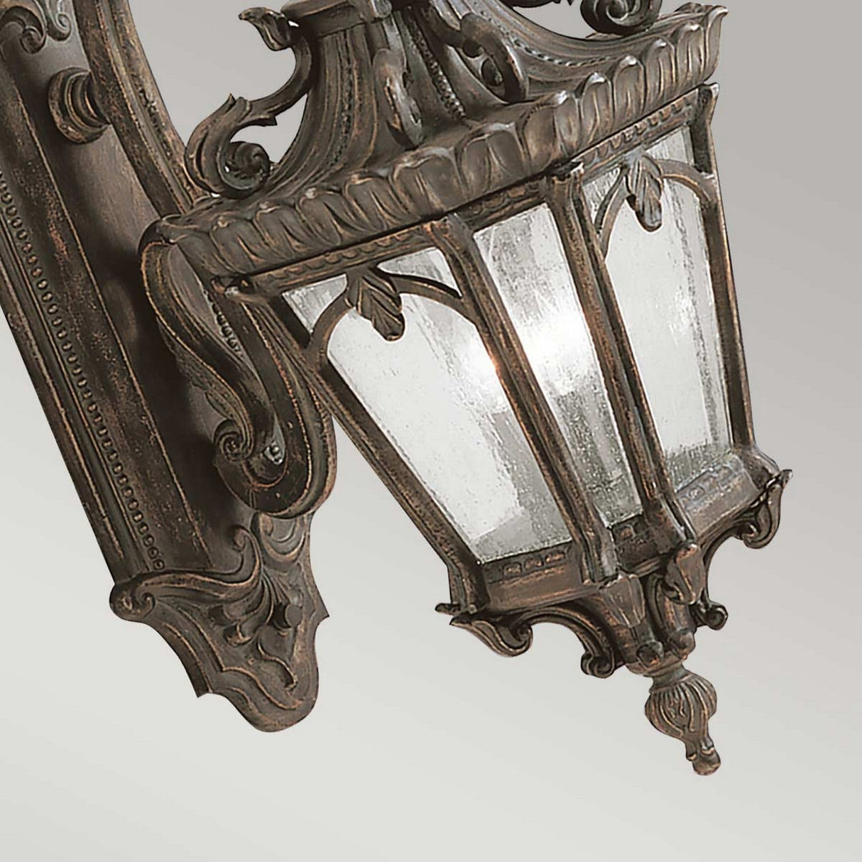 The Tournai Outdoor 3 Light Extra Large Wall Lantern in bronze showcases a vintage style with intricate scrollwork and seedy glass panels, all mounted on a decorative backplate, set against a plain background.