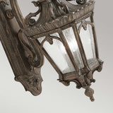 The Tournai Outdoor 3 Light Extra Large Wall Lantern in bronze showcases a vintage style with intricate scrollwork and seedy glass panels, all mounted on a decorative backplate, set against a plain background.