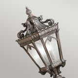 Set against a neutral background, the Tournai 2 Light Large Pedestal in bronze stands proudly with its vintage-style design. This outdoor fixture showcases ornate metalwork and clear seedy glass panels, featuring decorative scrolls and leaf patterns that exude an elegant and classical charm.