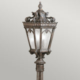 A Tournai 1 Light Medium Pillar - Bronze outdoor lamp post, featuring an ornate vintage-style design crafted from hand-cast aluminium with intricate decorative detailing and glass panels. Set against a simple background, it showcases a dark bronze finish reminiscent of classic designs.