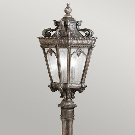A Tournai 1 Light Medium Pillar - Bronze outdoor lamp post, featuring an ornate vintage-style design crafted from hand-cast aluminium with intricate decorative detailing and glass panels. Set against a simple background, it showcases a dark bronze finish reminiscent of classic designs.