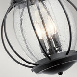 A close-up of the Vandalia Outdoor 3 Light Large Chain Pendant in black showcases its modern lantern design with a metal frame and clear bubbled glass, elegantly enclosing three lit bulbs. The curved metal bars contribute to the elegance of this IP44 weatherproof fixture.