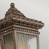 A detailed view of the Venetian Rain Outdoor 1 Light Half Wall Lantern reveals its decorative ornate metalwork and frosted glass panels. The lantern's textured brushed bronze finish exudes elegance with intricate detailing around the edges.
