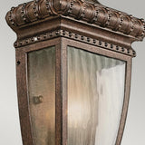 Close-up of the Venetian Rain Outdoor 1 Light Half Wall Lantern in brushed bronze, featuring clear glass panels. The gently glowing light inside accentuates the ornate detailing, evoking a gentle Venetian rain over its vintage-style frame.