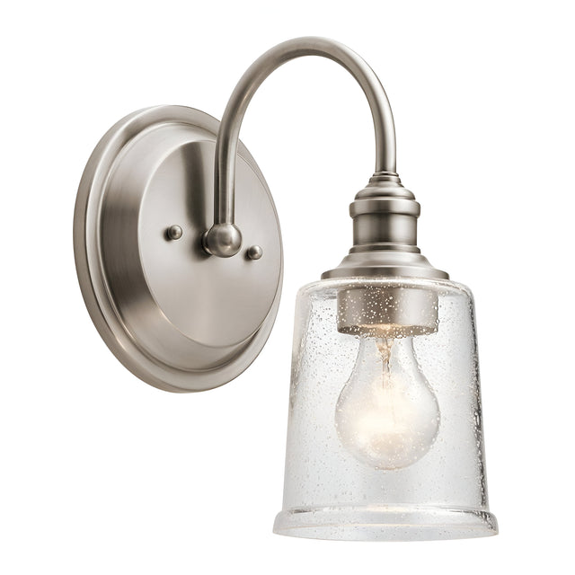 The Waverly 1 Light Wall Light - Silver is a wall-mounted fixture with a vintage-inspired design, featuring a brushed nickel finish and a curved arm. Its clear glass shade, adorned with small bubbles, elegantly displays the light bulb inside.