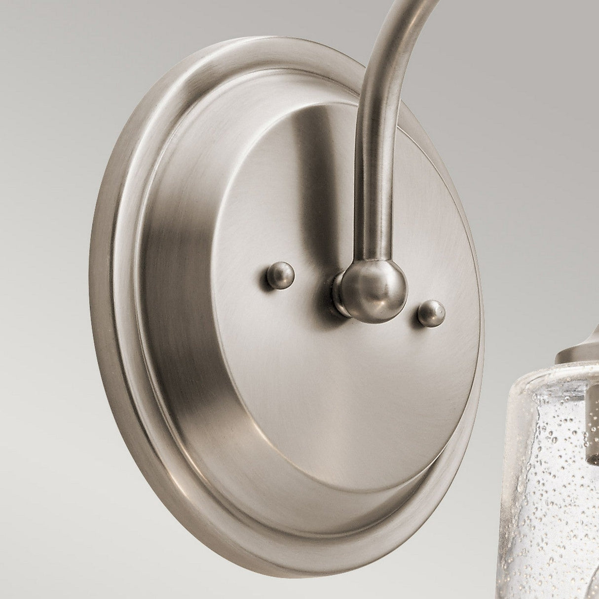 Here's a revised version of the sentence using the given product data:

A close-up view of the Waverly 1 Light Wall Light - Silver highlights its brushed nickel base and vintage-inspired curved arm that extends downwards. The smooth, circular base features two decorative round fasteners. This elegant wall sconce extends to a glass dome, partially visible on the right.