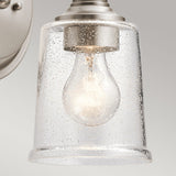 Detailed view of the Waverly 1 Light Wall Light - Silver, showcasing its vintage-inspired design with a clear glass shade adorned with small bubbles. The bulb inside emits a warm glow, and the silver metal fitting offers a modern contrast against the gray background.