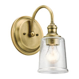 The Waverly 1 Light Wall Light in natural brass includes a clear, seeded glass shade that elegantly displays an exposed bulb. Its design, featuring a graceful curved arm and round backplate, enhances its vintage charm and adds a timeless touch to any decor.