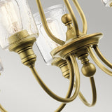 Close-up of the Waverly 5 Light Chandelier in natural brass: featuring multiple arms and seeded glass shades that reveal visible light bulbs. The sleek, curved metallic design creates a striking contrast with the textured glass, set against a light gray background.