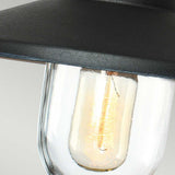 Close-up of the Klampenborg 1 Light Outdoor Wall Light in black, featuring a vintage-style bulb embraced by a clear glass casing and partially covered by a black metallic shade. The warm glow of the filament captures Scandinavian design principles, making it ideal for an outdoor wall light setting.