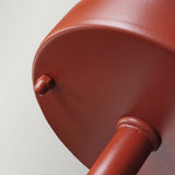 Close-up view of the Klampenborg 1 Light Outdoor Wall Light in oxide red, featuring a metal circular design with an attached cylindrical rod. The image highlights the smooth surface and connection point, emphasizing texture and color against a plain background, reminiscent of Scandinavian style.