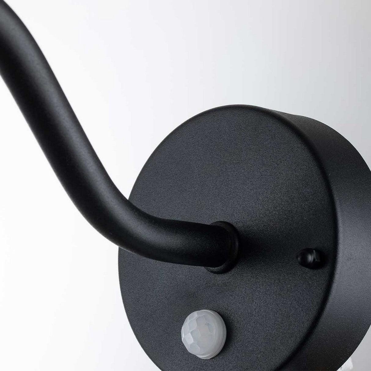 A close-up of the black Klampenborg 1 Light Outdoor Wall Light showcases its circular wall-mounted arm with a PIR sensor at the base. This elegant fixture, embodying Scandinavian design, gracefully curves outward from its round base against a plain white background.