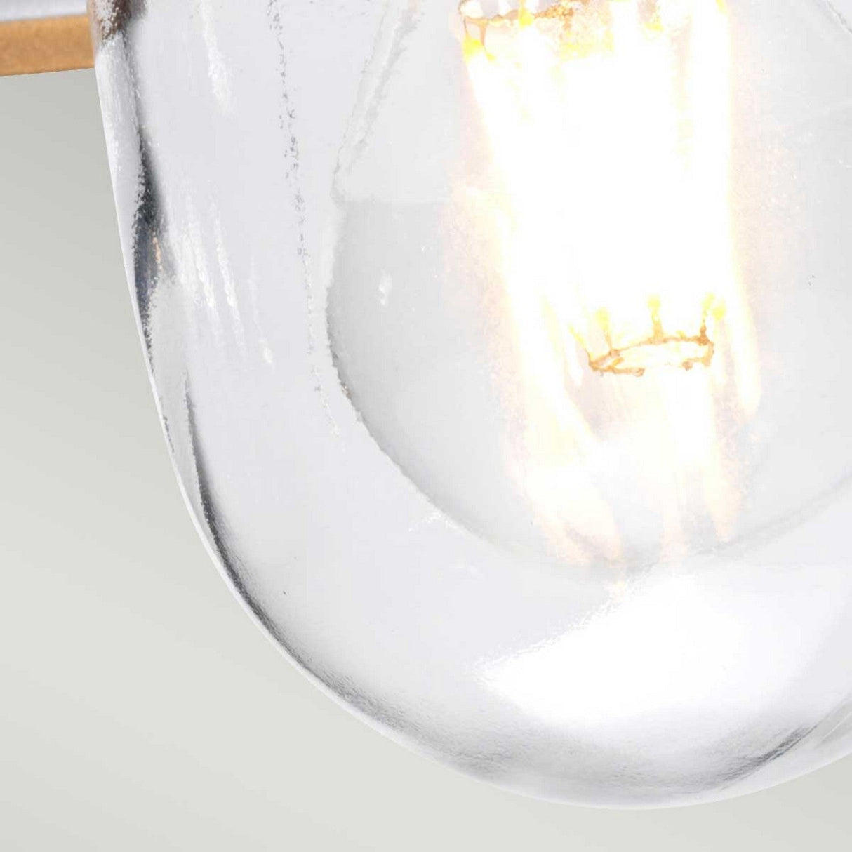 A close-up of the Klampenborg 1 Light Outdoor Chain Pendant reveals an illuminated vintage-style bulb. Its clear glass casing and glowing filament create a warm contrast against the light gray background, showcasing Scandinavian minimalism with a hint of stainless steel elegance.